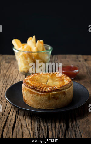 Une tarte de viande britannique traditionnel et frites assis sur une table en bois rustique. Banque D'Images