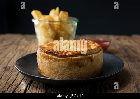 Une tarte de viande britannique traditionnel et frites assis sur une table en bois rustique. Banque D'Images