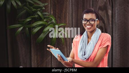 Digital composite of Smiling businesswoman using tablet PC contre le mur Banque D'Images