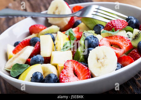 Bol de salade de fruits avec les fraises, les bleuets, les pommes, les kiwis, les bananes en tranches, salade de fruits d'été saison saine assortiment Banque D'Images