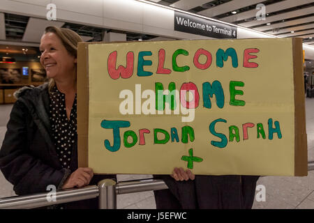 Une mère est titulaire d'un signe de bienvenue à la maison de son fils qui est de retour de voyage, l'aéroport de Heathrow, Londres, UK Banque D'Images