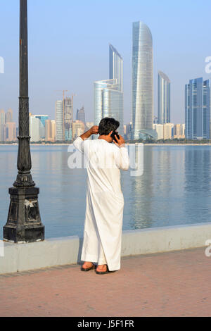 Vue sur l'horizon d'Abu Dhabi avec un homme vêtu de vêtements traditionnels arabes à l'aide d'un téléphone mobile, Emirats arabes unis (EAU), Moyen-Orient Banque D'Images