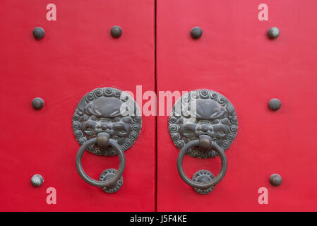 Poignées de porte tête de lion sur une porte en bois cloutée rouge sur blanc Cloud temple bouddhiste à Shanghai, Chine Banque D'Images