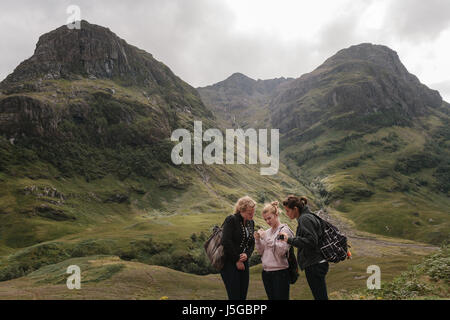 Trois belles femmes touristes regardant des photos sur leur smartphone avec les montagnes derrière elles à Glencoe, en Écosse. Banque D'Images