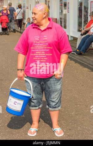 Une femme chauve portant un t-shirt rose de la collection pour le cancer Macmillan Cancer Support sur la jetée sur Herne Bay seafront, Kent. Banque D'Images