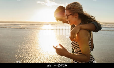 Vue de côté tourné de jeune couple aimant profiter d'une journée sur la plage. Belle femme avec son petit ami marche sur la mer un jour d'été. Banque D'Images