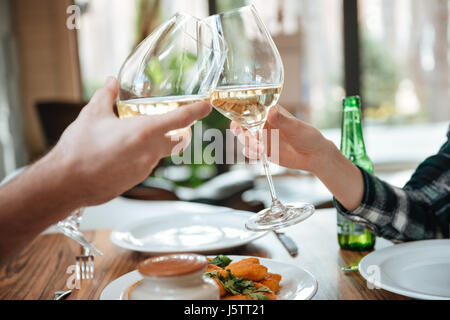 Close up portrait of a female and male hands toasting avec verres de vin blanc sur le tableau Banque D'Images