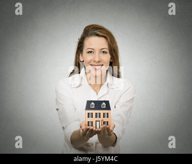 Portrait happy smiling woman presenting petit modèle de maison, mur gris isolé. Visage humain positif expressions, émotions, sentiments. Rea Banque D'Images