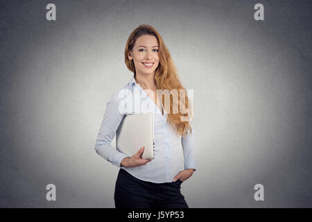 Portrait young beautiful happy woman holding laptop smiling standing bureau isolé sur fond de mur gris. Expression visage positif de l'émotion. Comput Banque D'Images