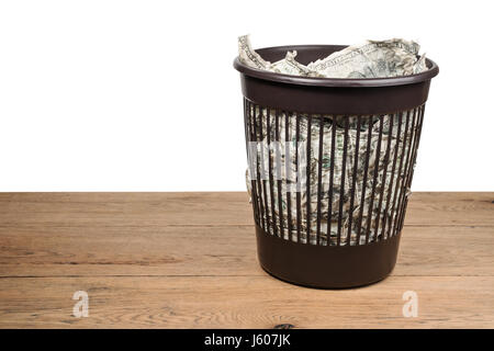 Garbage panier plein de dollars froissés se dresse sur une vieille table en bois isolé sur fond blanc Banque D'Images