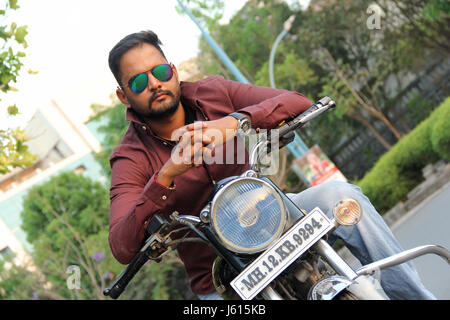 Jeune Indien homme avec lunettes fantaisie reposant sur moto et looking at camera Banque D'Images