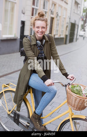 Portrait of smiling young woman riding bicycle avec produire dans panier Banque D'Images