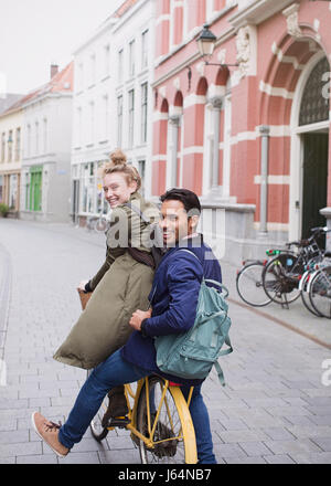 Portrait of smiling young man and woman riding bicycle on city street Banque D'Images