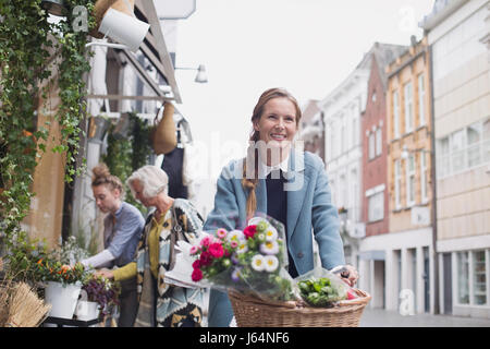 Smiling woman riding bicycle avec des fleurs dans un panier on city street Banque D'Images