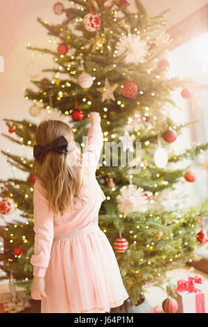 Fille en robe rose hanging ornaments on Christmas Tree Banque D'Images