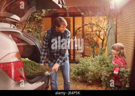 Père et fille de l'arbre de Noël de déchargement à partir de la voiture à l'extérieur chambre Banque D'Images