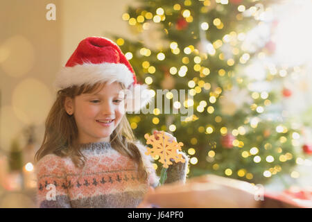 Girl in Santa hat holding snowflake ornament in front of Christmas Tree Banque D'Images