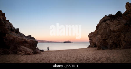 Deux amoureux sur une plage avec un bateau de croisière dans l'arrière-plan. Banque D'Images