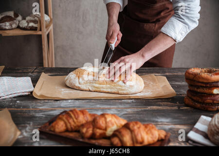 Portrait de jeune homme baker debout à couper le pain de boulangerie. Banque D'Images