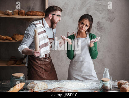 Homme barbu en colère en criant à sa femme lunettes tablier de cuisine en cuisine pendant qu'ils Banque D'Images