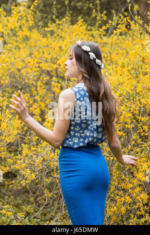 Belle jeune fille rêveuse dans spring park. Bush avec des fleurs jaunes sur fond. Banque D'Images