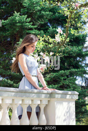 Belle dame debout sur un balcon du palais près de magnolia arbre sur un jour ensoleillé. Vent souffle ses cheveux Banque D'Images