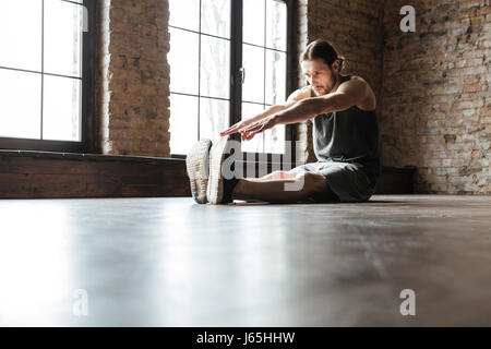 Portrait d'un sportif en bonne santé faisant des exercices d'étirement en position assise sur le sol dans la salle de sport Banque D'Images