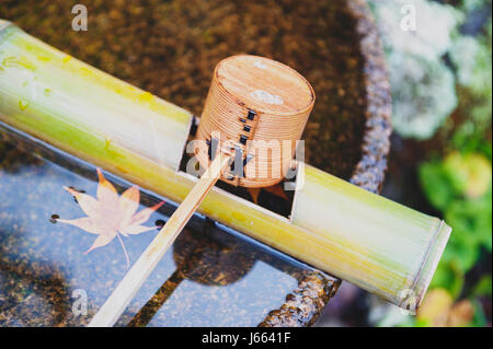 Balancier de purification en bois japonais dans un bassin d'eau ou chozubachi utilisée pour rincer les mains en japonais, temples, sanctuaires et jardins. Banque D'Images