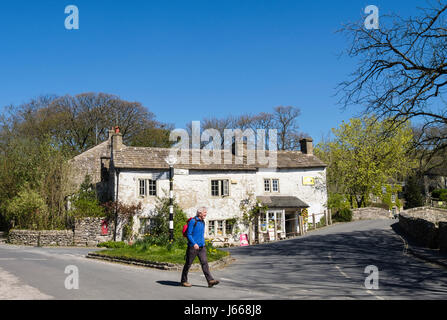 Un randonneur marchant passé ancienne boutique et panneau à la jonction de route dans le centre du village. Malham Yorkshire Dales National Park North Yorkshire Angleterre Royaume-uni Grande-Bretagne Banque D'Images