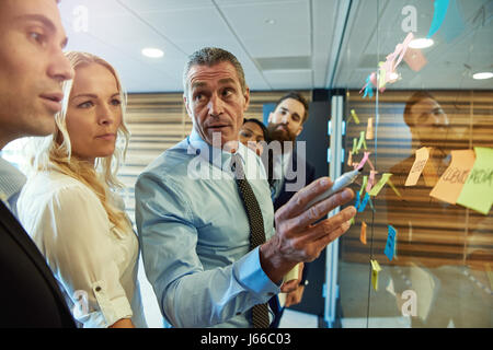 Businessman lors d'une réunion avec des collègues regroupés autour des idées sur des notes collantes à côté avec une expression attentive comme il écoute une équipe membres Banque D'Images