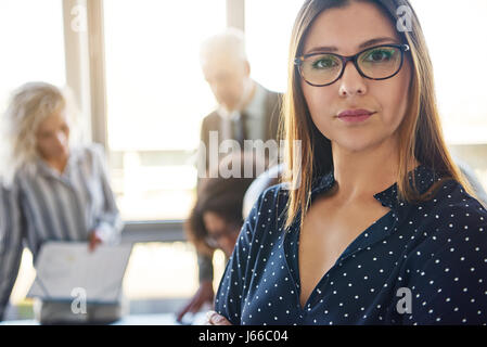 Femme d'affaires graves devant team in office, looking at camera Banque D'Images