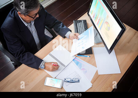 L'homme d'affaires à la recherche d'entreprises le rapport graphique du papier dans la main et le plan d'analyse de la stratégie d'écriture sur la table de travail Banque D'Images