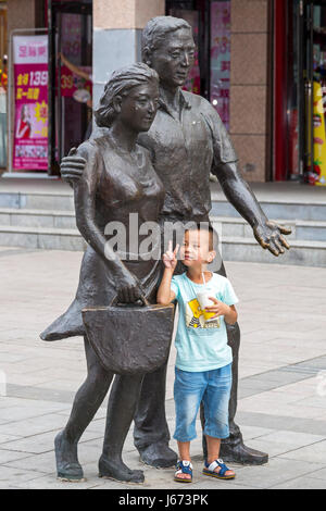 Enfant posant enfant de statue de couple dans la rue commerçante, Yinchuan, Ningxia, Chine Banque D'Images