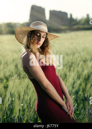 Jeune fille blonde à l'extérieur. Avec chapeau et robe rouge dans le champ de blé. Rétro-éclairée. Banque D'Images