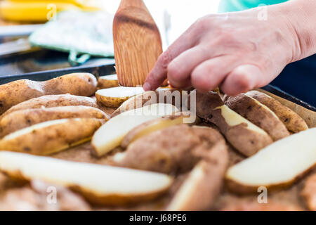 Gros plan macro de womans mains flipping ou la restitution de pommes de terre frites Nature au four Banque D'Images