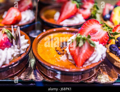 Gros plan macro de golden pots crème brûlée avec fraises et crème fouettée à l'écran en verre derrière boulangerie Banque D'Images