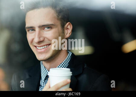 Portrait of handsome young man looking at camera et jetables smiling holding Coffee cup in cafe Banque D'Images