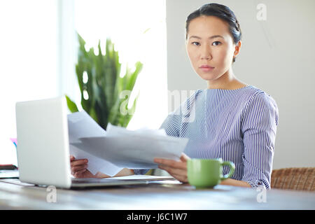 Portrait de jeune femme vêtue de vêtements décontractés, travaillant avec un ordinateur portable dans un bureau moderne à la caméra au sérieux Banque D'Images