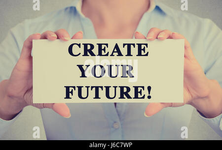 Young hands holding white card signe avec créer votre futur message texte isolé sur fond de bureau mur gris. Image retro style instagram Banque D'Images