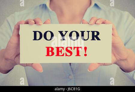 Young hands holding white card signe avec faire votre meilleur message texte isolé sur fond de bureau mur gris. Image retro style instagram Banque D'Images