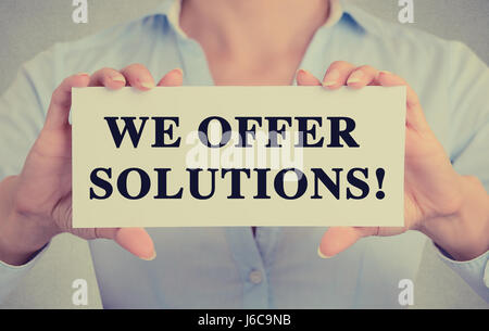 Young hands holding white card signer avec nous offrons des solutions ! Message texte isolé sur fond de bureau mur gris. Image retro style instagram Banque D'Images