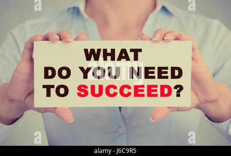 Young hands holding white card signer avec ce que vous avez besoin pour réussir question message texte isolé sur fond de bureau mur gris. Retro inst Banque D'Images