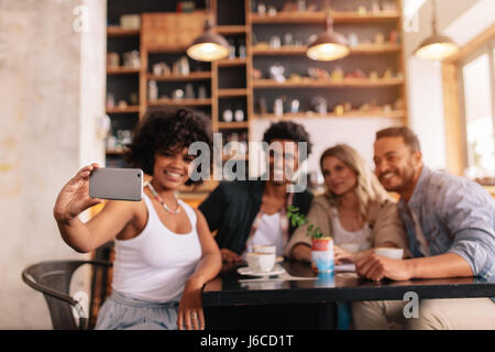 Groupe multiracial d'amis prenant sur selfies smart phone at coffee shop. Les jeunes, hommes et femmes, assis à table et de prendre un café self portrait avec mo Banque D'Images