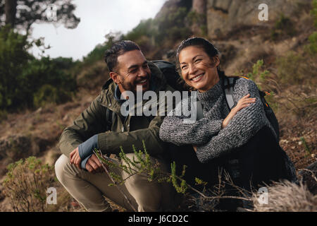 Jeune couple en faisant une pause sur une randonnée. Heureux jeune homme et femme assis sur sentier de montagne. Banque D'Images