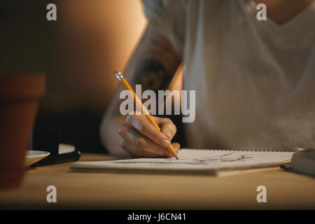 Photo recadrée de jeune femme designer assis à l'intérieur la nuit à écrire des notes. Banque D'Images