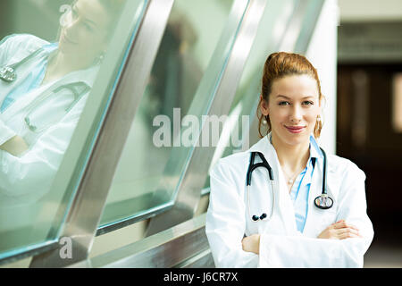 Closeup portrait jeune, souriant, confiant, femme médecin, professionnel de la santé avec stéthoscope, permanent à la recherche à l'hôpital d'arrière-plan vous avez isolé Banque D'Images