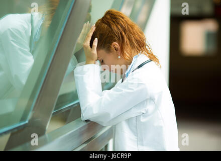 Closeup portrait professionnel de la santé avec des maux de tête, a souligné, en maintenant la tête contre la fenêtre en verre. Infirmière Médecin migraineux surmenés, overstre Banque D'Images