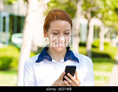 Closeup portrait heureux, joyeux, fille, excité par ce qu'elle voit sur téléphone cellulaire extérieur isolé bureau corporative. L'expression faciale reactio Banque D'Images