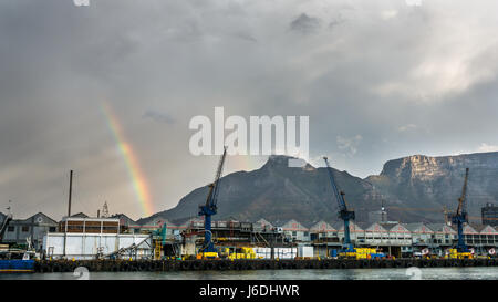 Table Mountain et Devil's Peak avec un double arc-en-ciel derrière des grues dans un chantier naval et un ciel sombre de tempête, Victoria Basin, le port du Cap, Afrique du Sud Banque D'Images