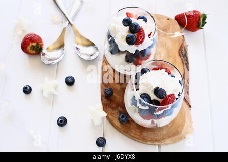 Bagatelles faite avec des bleuets, des fraises, de la crème fouettée et des gâteaux en forme d'étoile livre contre un arrière-plan en bois blanc. Parfait pour les quatrième de juillet. Sha Banque D'Images